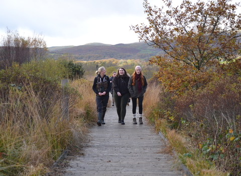 Three volunteers walking towards camera along a boardwalk in a wetland