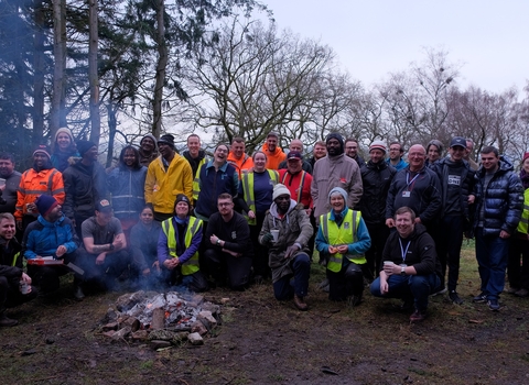A group of volunteers gathered around a campfire after a morning spent clearing rhododendron in Nercwys