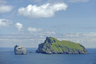 Boreray and Stac Lee, a pair of islands isolated in a calm blue sea. The larger island has grass growing on it's surface, though both have steep rocky sides and large cliff faces.