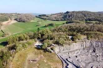 An arial view of Aberduna nature reserve. With a quarry area front right, lots of wooded ground with a few buildings hidden within. surrounded by fields and hills in the background.