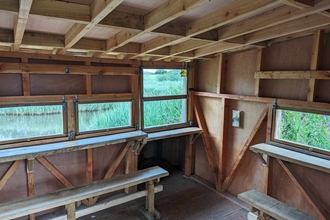 Photo of the inside of the Viley Hide at the Spinnies Aberogwen Reserve. There are two benches to sit on and several viewing windows out into the lagoon.