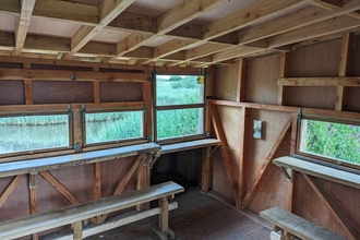 Photo of the inside of the Viley Hide at the Spinnies Aberogwen Reserve. There are two benches to sit on and several viewing windows out into the lagoon.