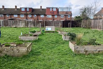 Raised beds surrounded by grass and a bench. Houses can be seen in the background. 
