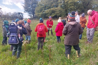 Jules cooper leads a group of foragers. They are stood in a field, wearing waterproofs and warm clothing.