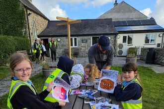 Children with hi-vis jackets and artwork, sitting around picnic bench in sunshine. 