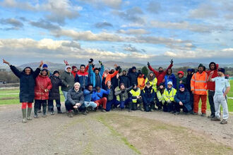 A group of people standing in a big landscape, smiling with hands in the air.