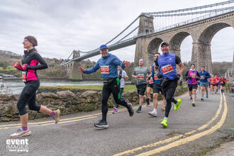 People running on road with Menai Bridge in backround. 