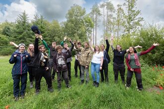 Group of young people in clearing in wood. They are all raising their arms in celebration. 