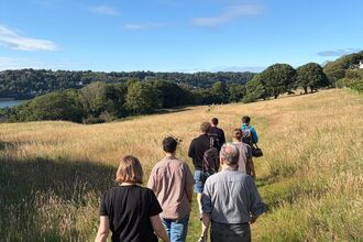 A group of people walking through a grassland, woodland on the horizon, blue sky