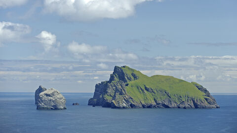 Boreray and Stac Lee, a pair of islands isolated in a calm blue sea. The larger island has grass growing on it's surface, though both have steep rocky sides and large cliff faces.