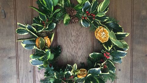 A handmade Christmas wreath, with holly and other evergreen leaves, dried orange slices, bright red berries, and pinecones. 