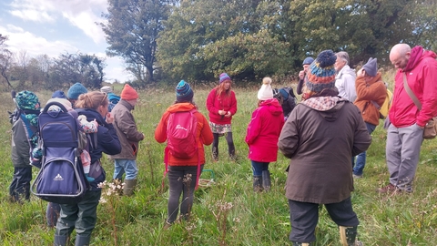 Jules cooper leads a group of foragers. They are stood in a field, wearing waterproofs and warm clothing.