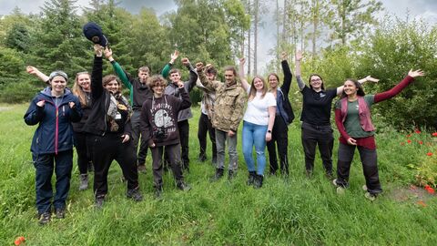 Group of young people in clearing in wood. They are all raising their arms in celebration. 