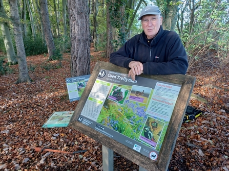 Graham Platt standing behind a reserve sign in a forest, surrounded by fallen autumn leaves