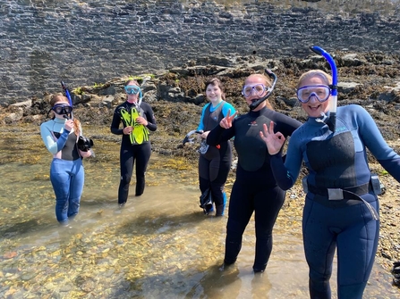 5 people stand in shallow water in snorkelling gear, posing for the camera