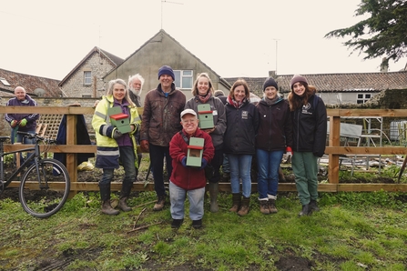 Volunteers pose with bird boxes outside in a community garden.