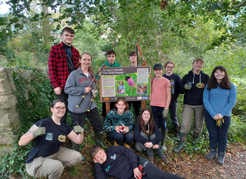 Group of young people with garden tools standing proudly in front of an information sign