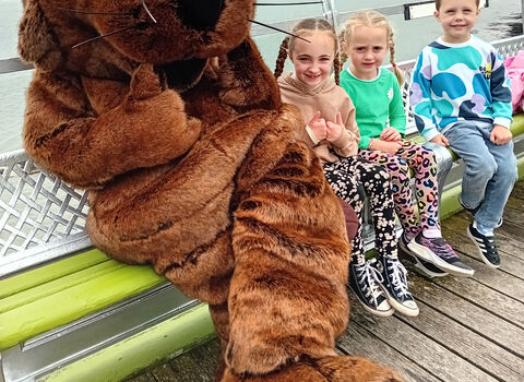 Person in beaver suit sitting on a bench with children