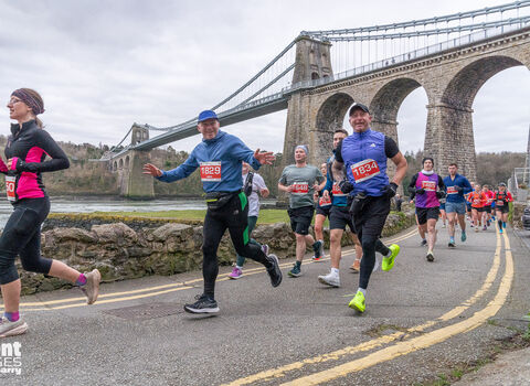 People running on road with Menai Bridge in backround. 