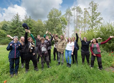Group of young people in clearing in wood. They are all raising their arms in celebration. 